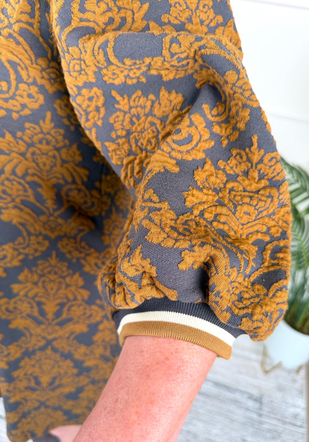 Close-up of a person wearing a gray knit top with a bold mustard yellow damask pattern and a ribbed tan, white, and gray cuff.