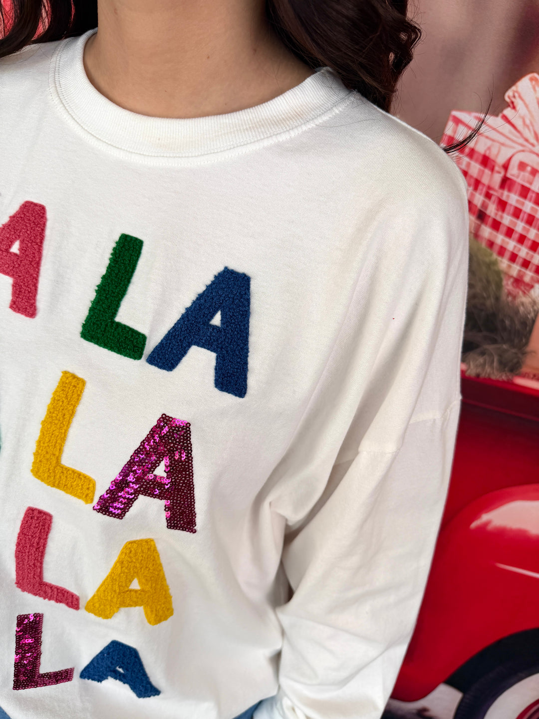 close up of white sweatshirt with colorful fa la la applique and sequins