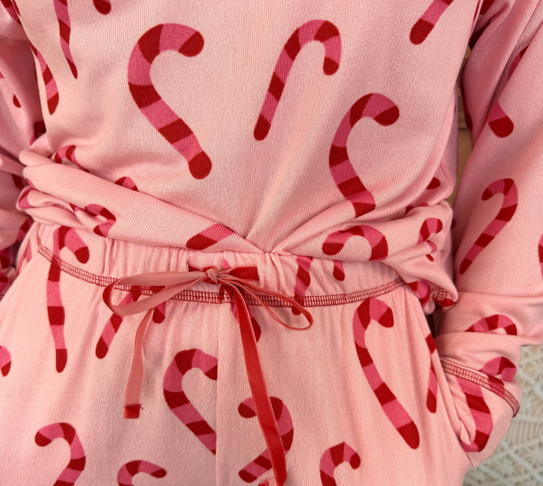 A close-up of a pink long-sleeve robe or pajama top with a red and pink candy cane pattern, featuring a matching drawstring tie at the waist.