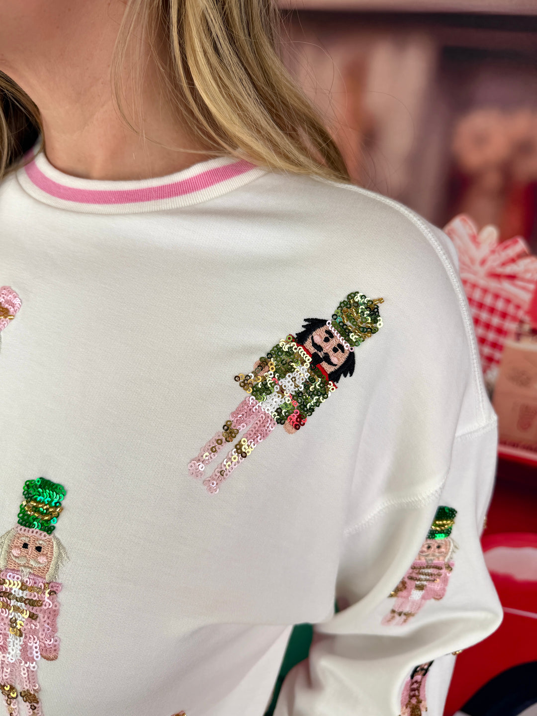 A close-up of a person wearing a white crewneck sweatshirt with pink trim and sequined nutcracker figures on the front.