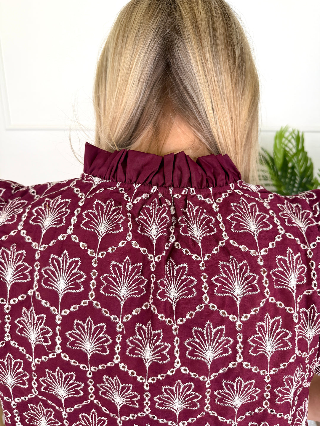 Back view of a woman wearing a maroon blouse with a white floral and chain pattern, featuring a gathered high neck.