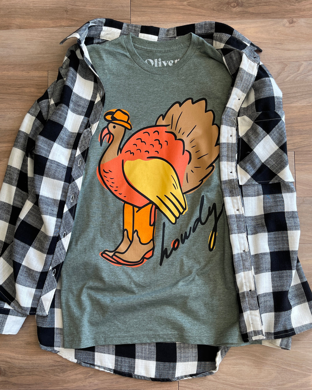 green tee, with hand drawn turkey in cowboy boots and text Howdy, paired with black and white flannel (items sold separately)
