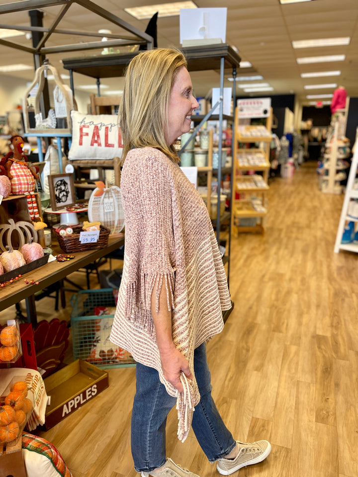 poncho style sweater with pink and cream striping and fringe at edges