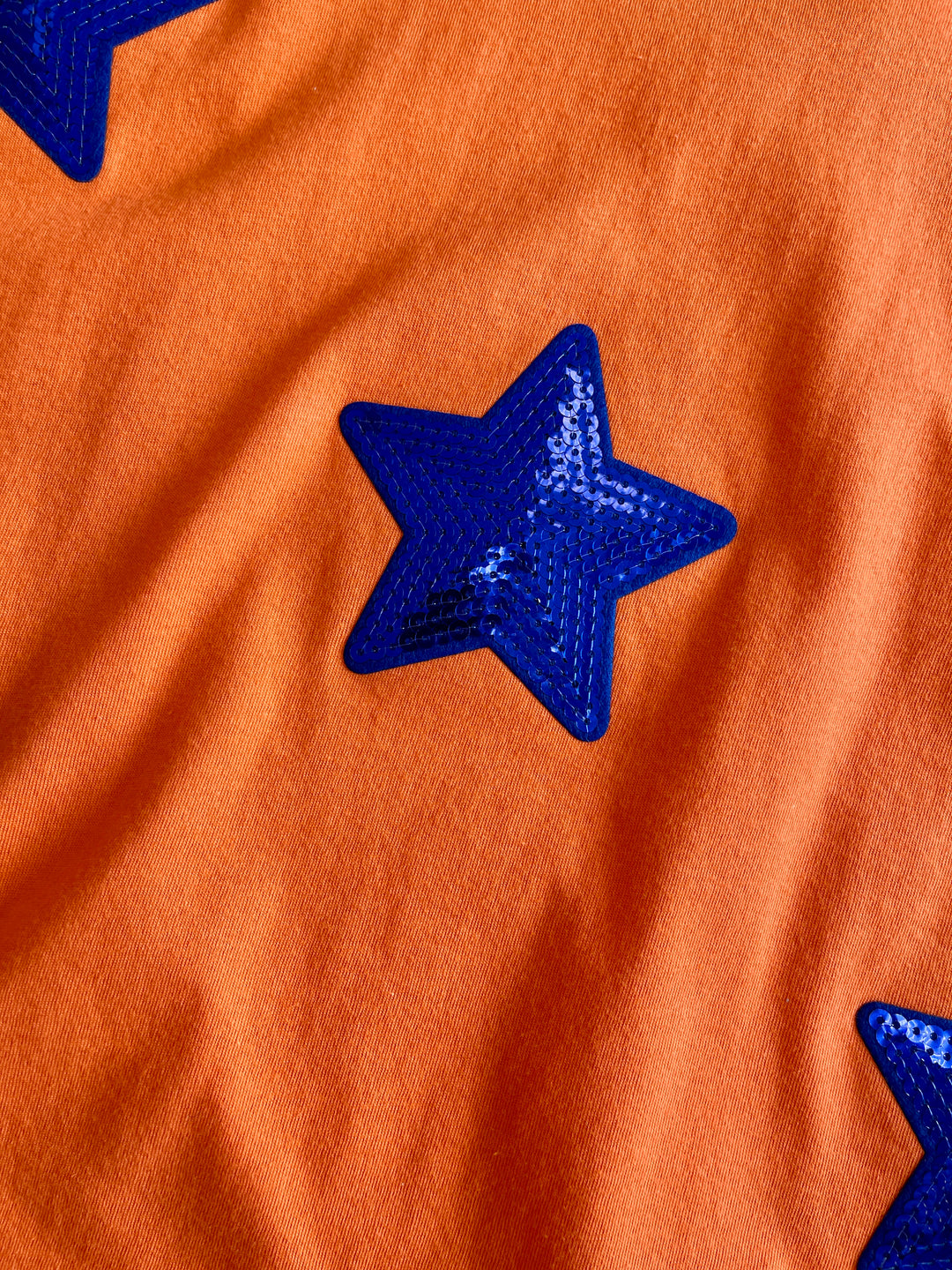 orange tee with royal blue iridescant stars sewn onto front of tee, short sleeve tee
