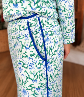 A close-up of a person wearing a matching pajama set with a white base, green and blue floral and scroll pattern, and a bright blue drawstring waist.